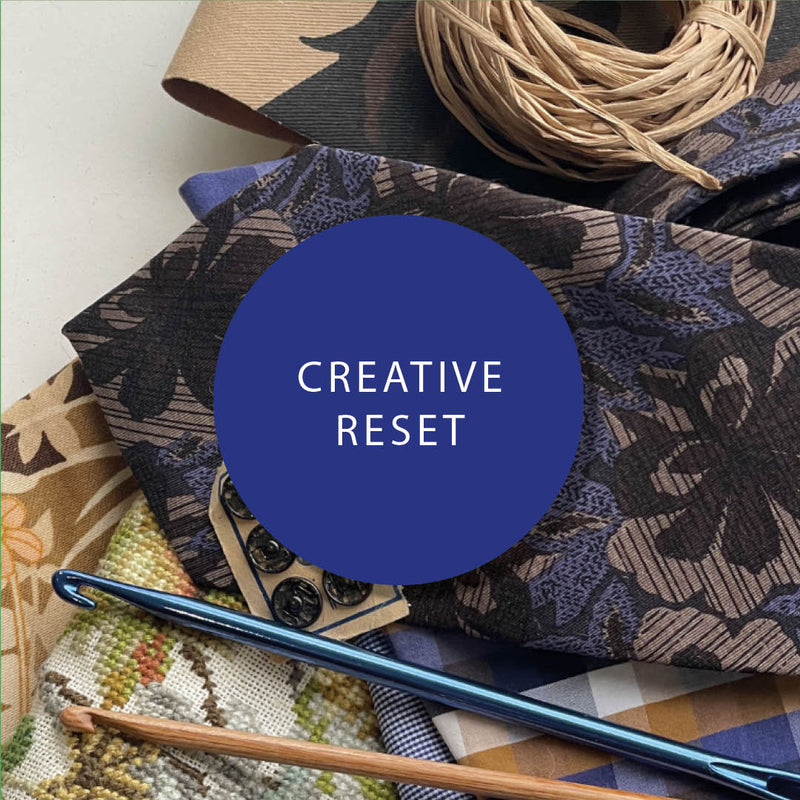 Creative reset embroidery and crochet supplies with patterned fabrics and blue crochet hook on a neutral background