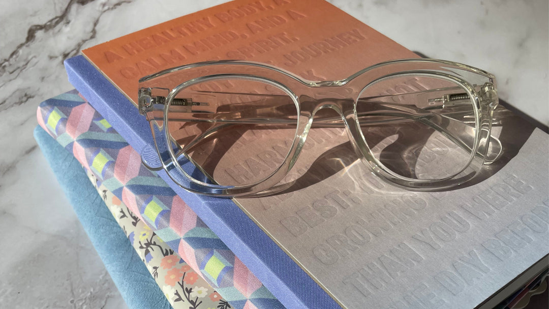 a stacjk of colourful notebooks with reading glasses on a marble table