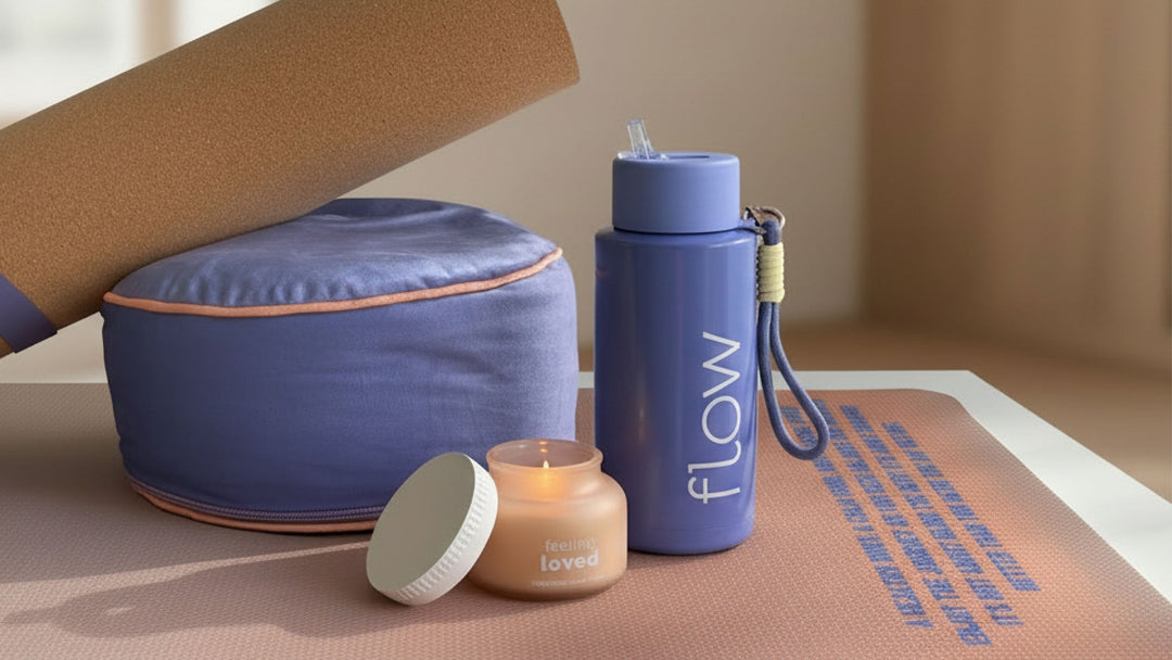 Blue yoga meditation cushion with cork yoga block, blue reusable water bottle with strap, small scented candle and yoga mat arranged as a wellbeing set