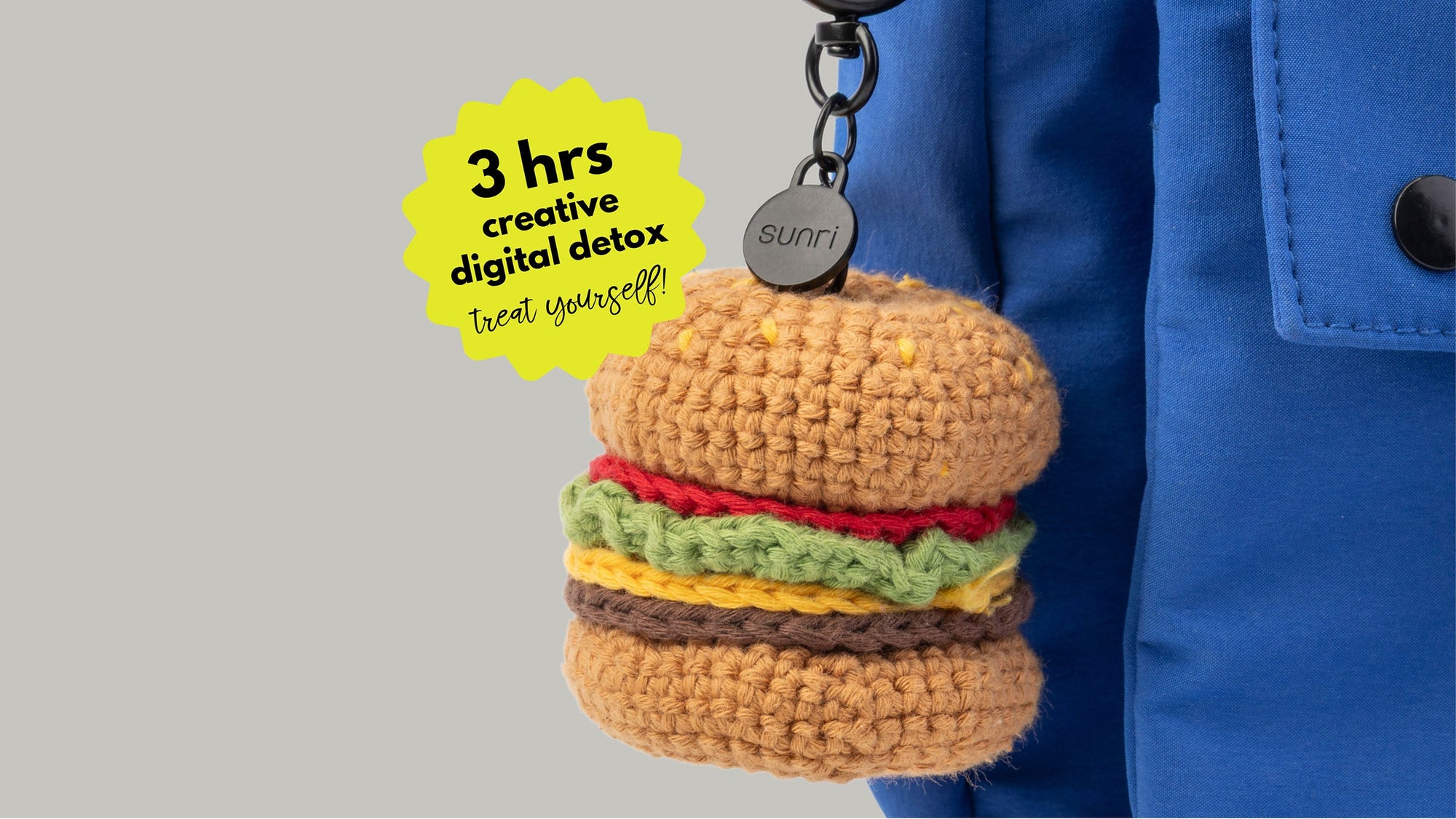 crocheted hamburger keychain with layered bun lettuce cheese and patty hanging from metal clip on blue fabric bag