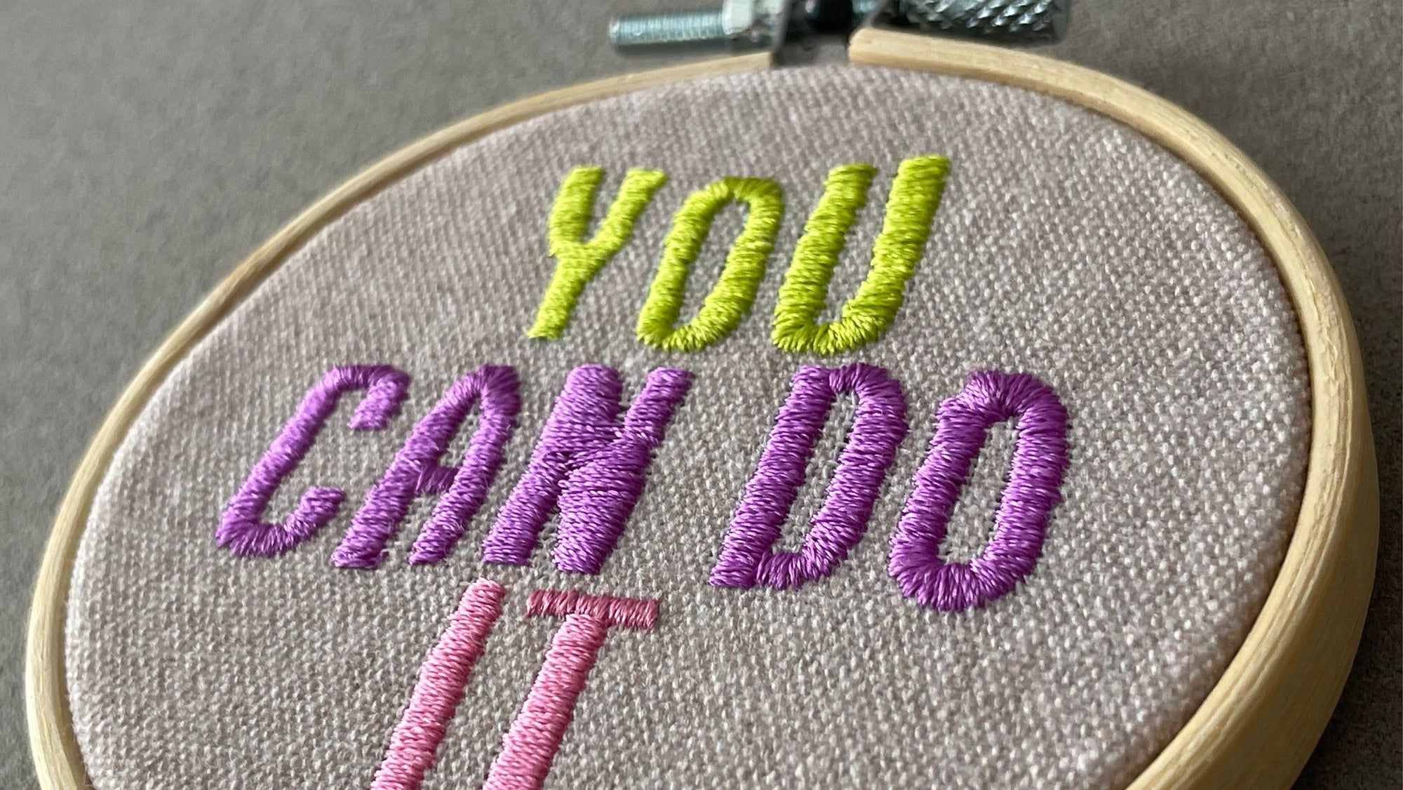 embroidered fabric hoop with stitched text you can do it in green purple and pink thread on natural fabric