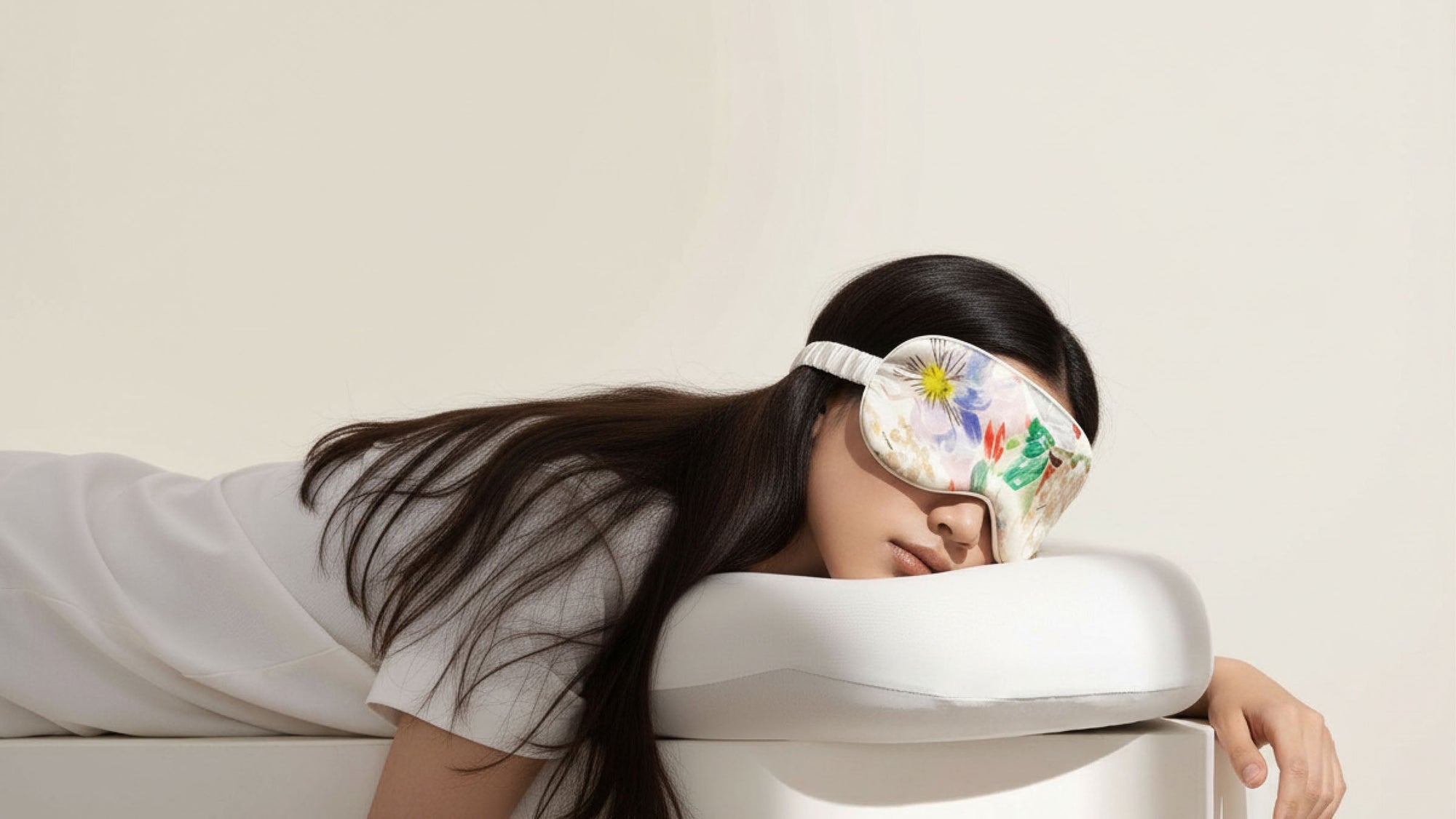 sleep mask with floral print worn over eyes, adjustable elastic strap, soft padded shape, model lying down