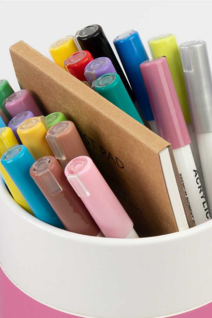 Close-up of acrylic marker tops in assorted colours with the artist pad behind
