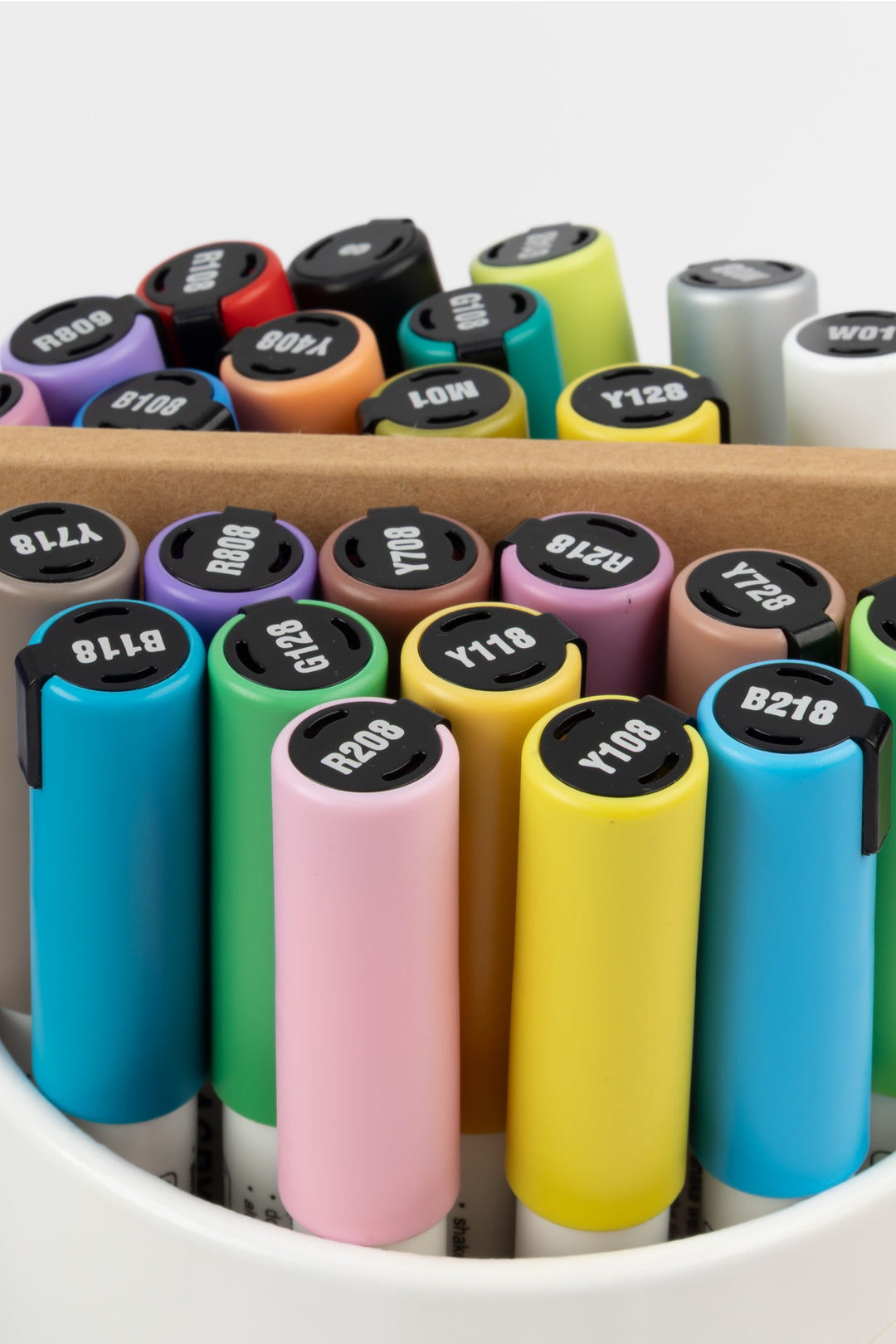 Close-up of acrylic marker tops in assorted colours with the artist pad behind
