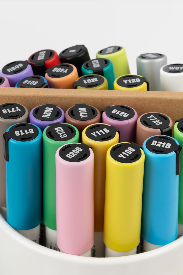 Close-up of acrylic marker tops in assorted colours with the artist pad behind
