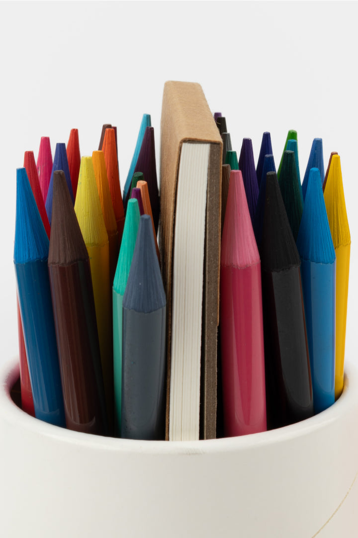 Close-up of woodless aquarelle pencils in assorted colours with the artist pad behind
