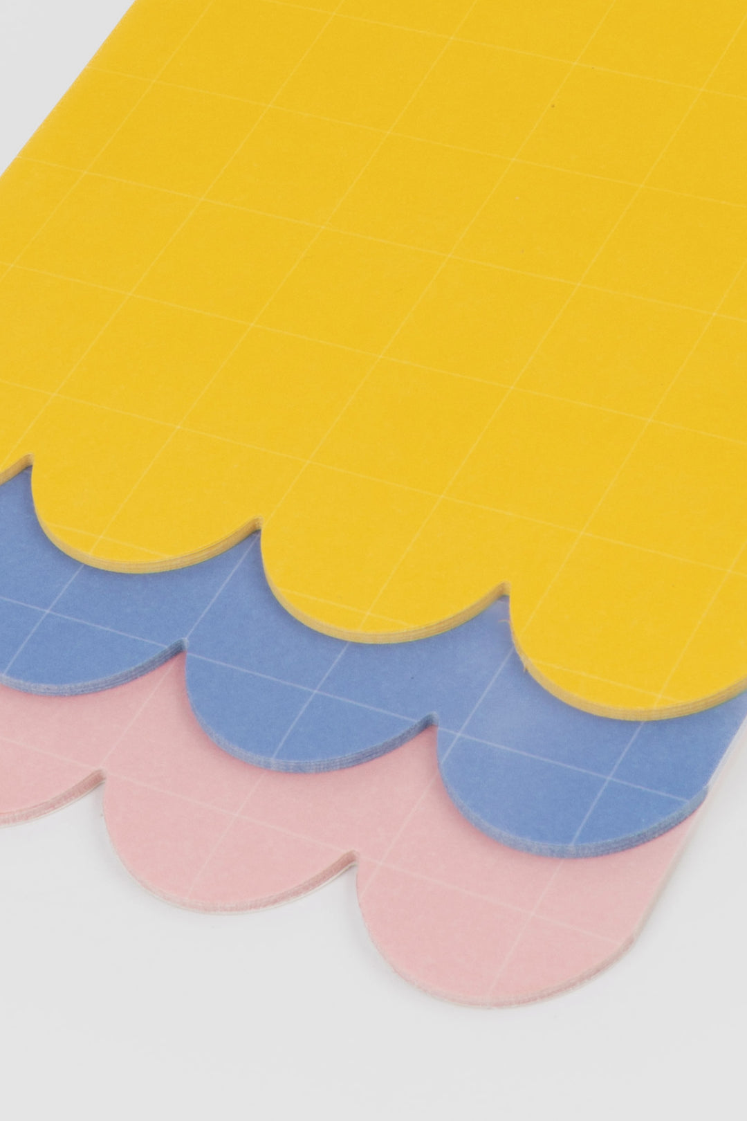 close up of yellow, blue and pink scalloped notepad sheets with grid pattern
