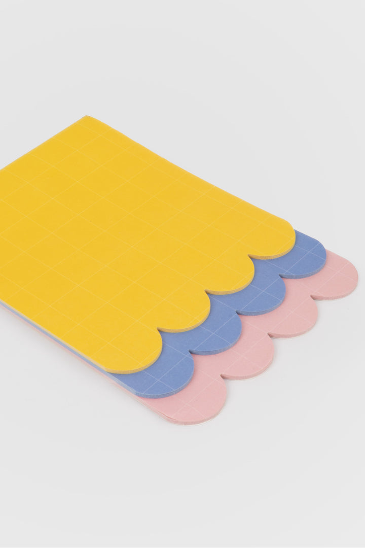 yellow scalloped notepad sheet with grid pattern and blue and pink layers underneath
