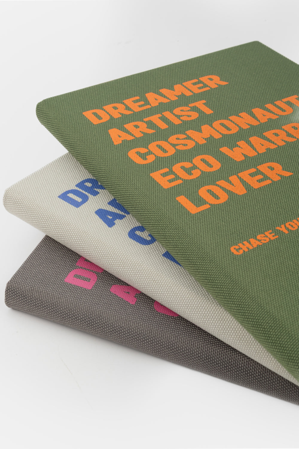 Stack of three fabric cover diaries in green beige and grey with printed text
