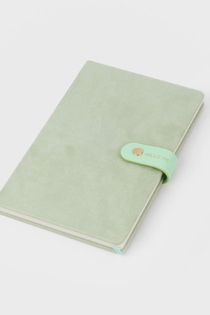 front view of a mint faux-suede notebook with a rounded flap closure with gold button detail and hello me text