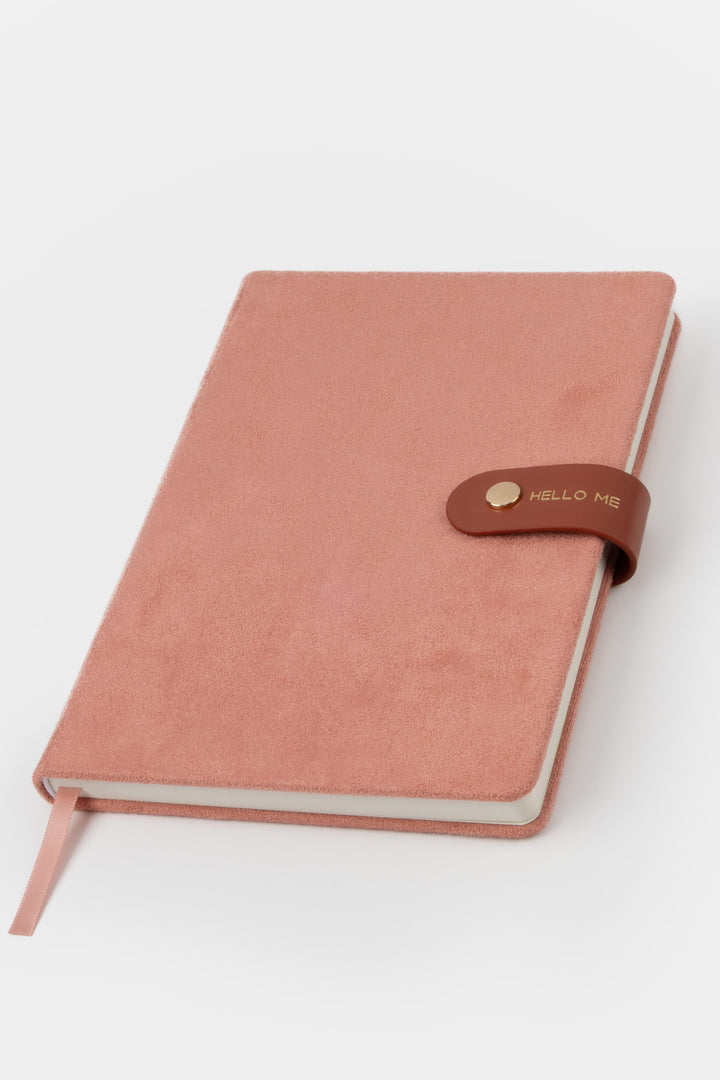 front view of a pink faux-suede notebook with a rounded flap closure with gold button detail and hello me text