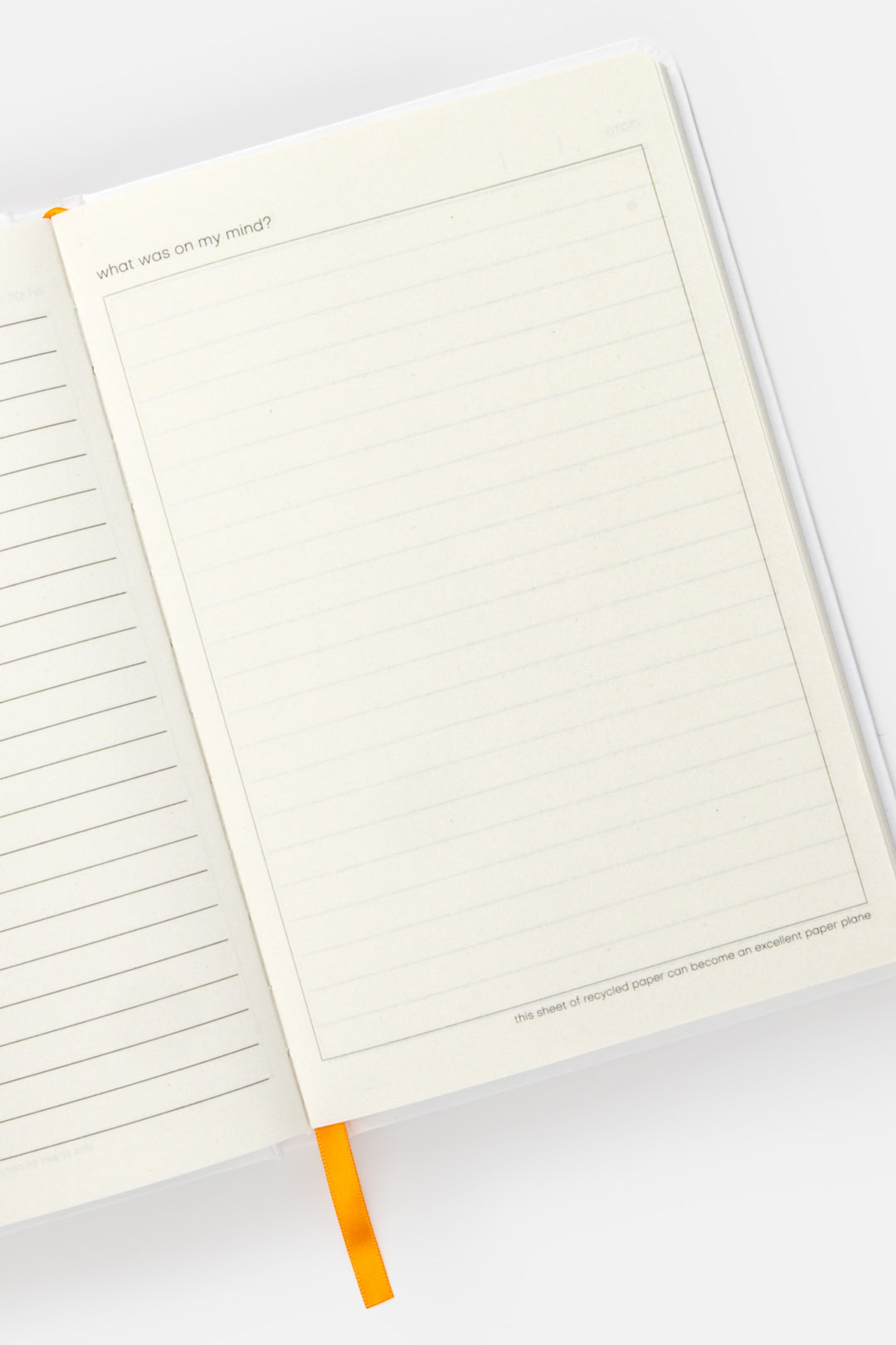 open daily diary showing lined recycled paper with orange ribbon marker

