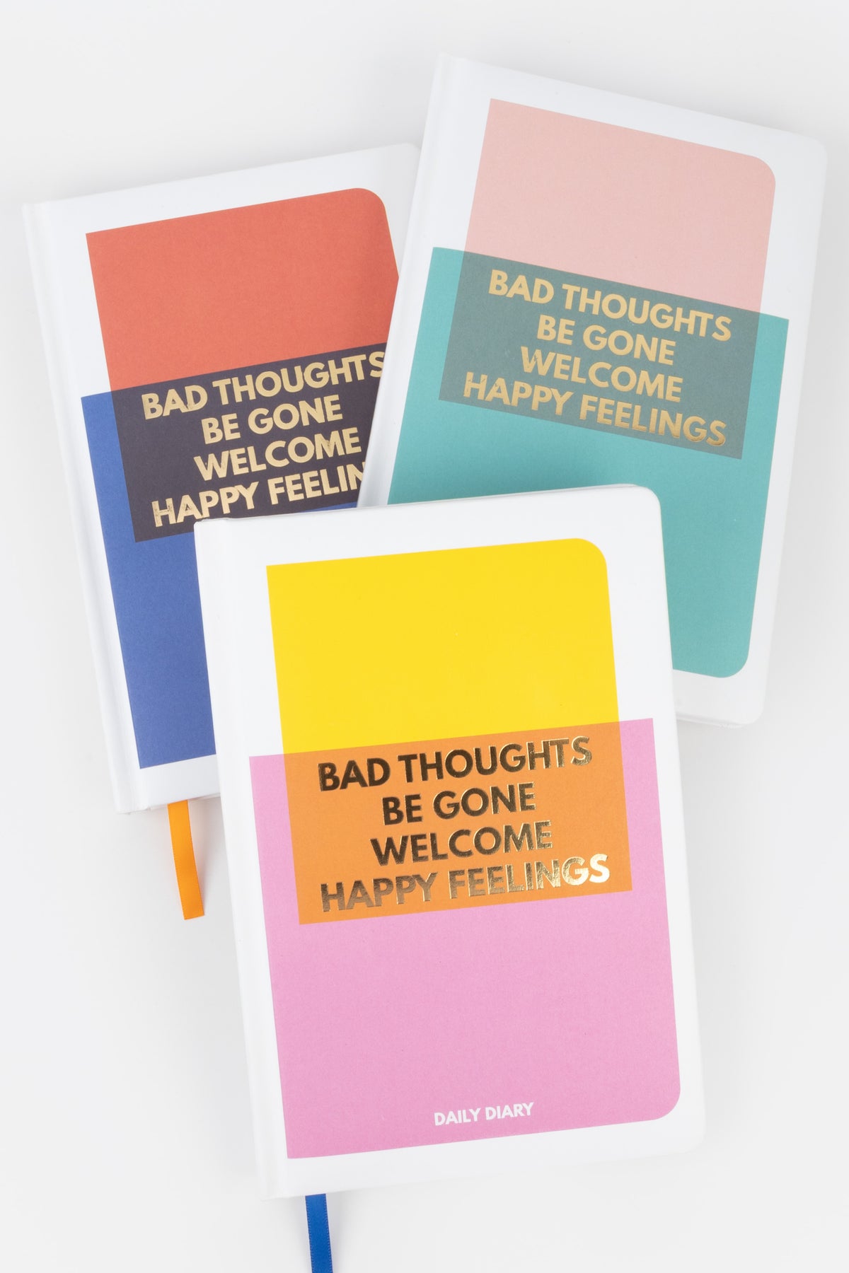 Three colourful diaries stacked with gold foil text on the covers
