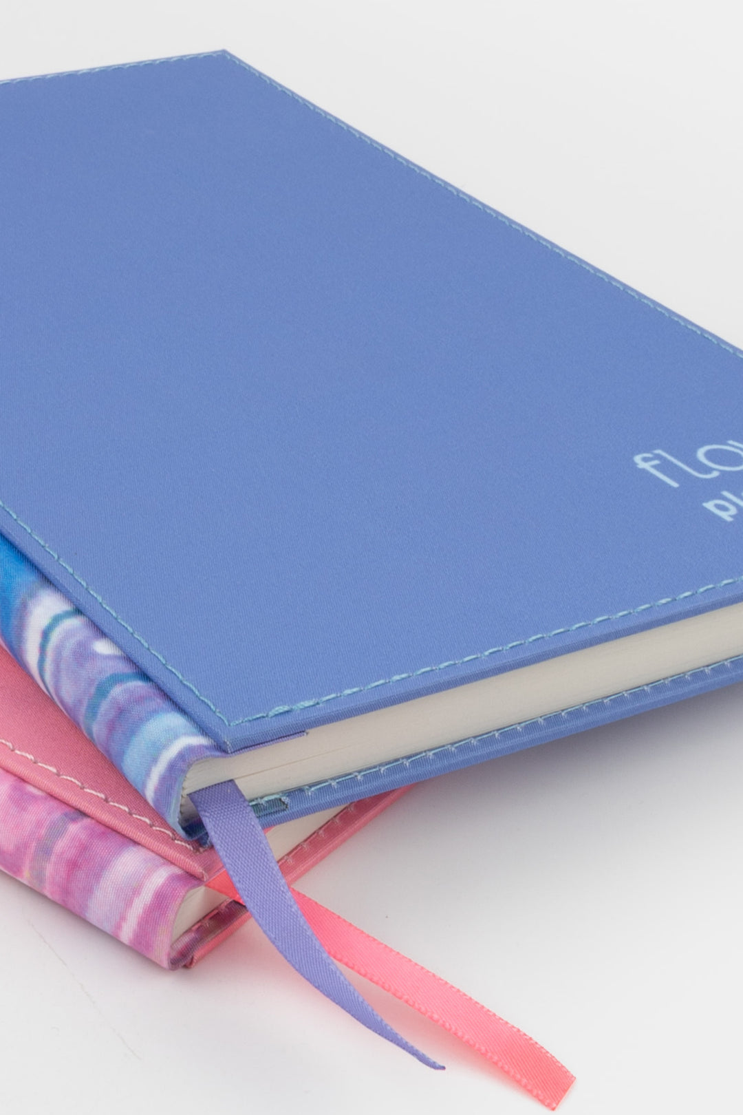 close-up of the blue planner stacked over the pink one with visible marbled spines and ribbon markers
