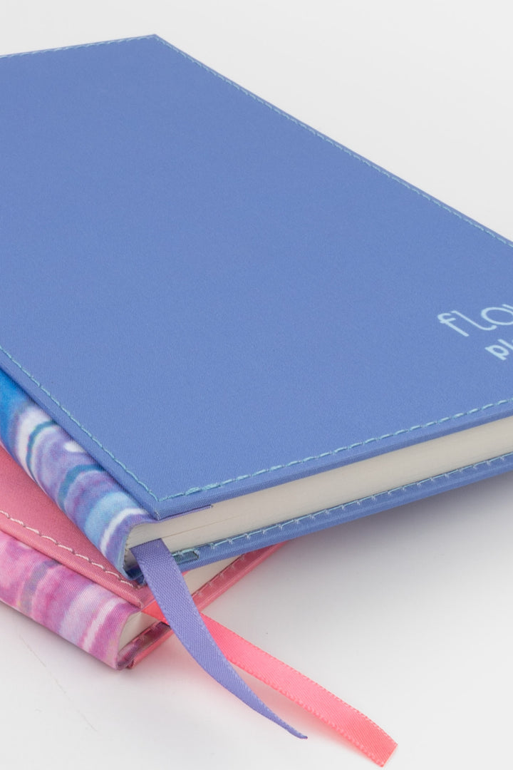 close-up of the blue planner stacked over the pink one with visible marbled spines and ribbon markers
