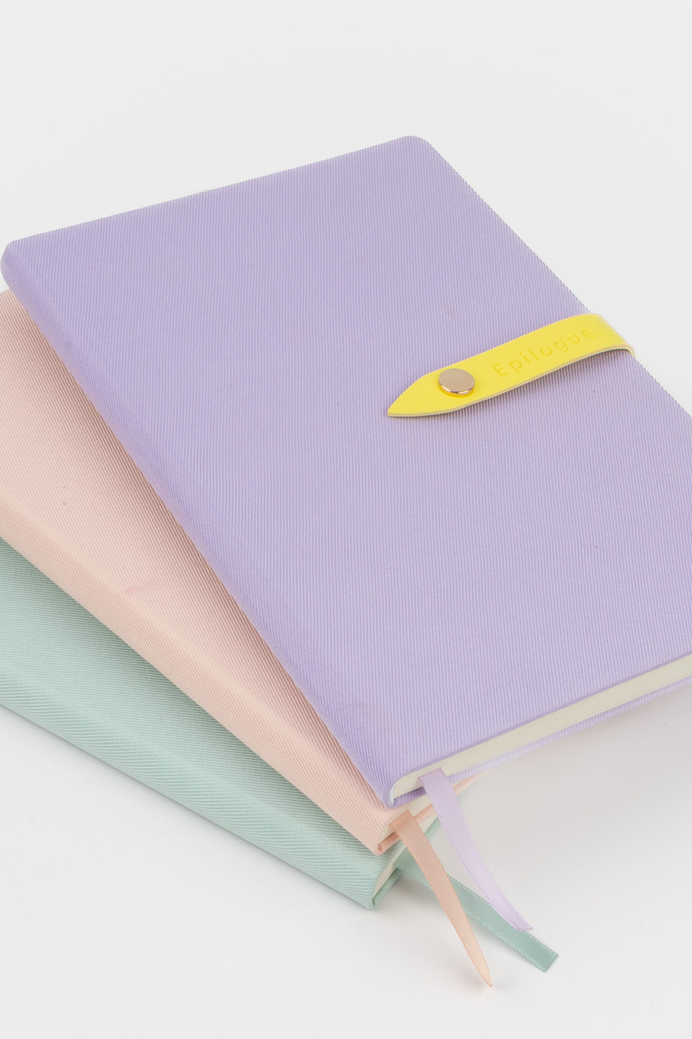 Three journals in pastel colors with a yellow strap on a light background