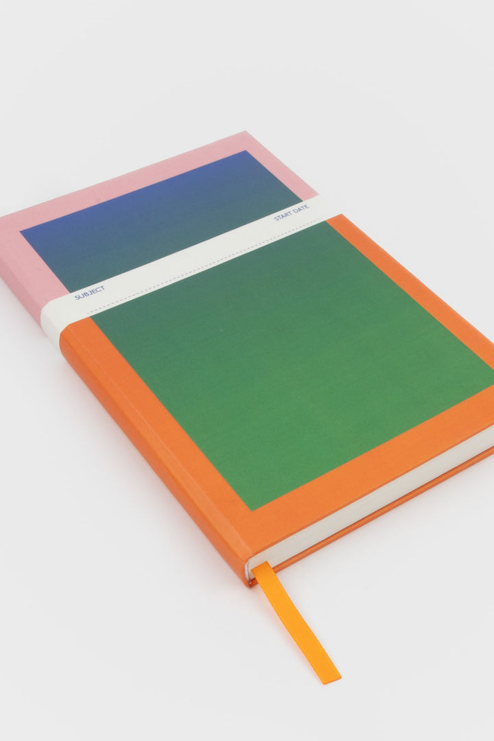 angled view of A5 notebook with orange border and blue-to-green gradient cover and orange satin marker
