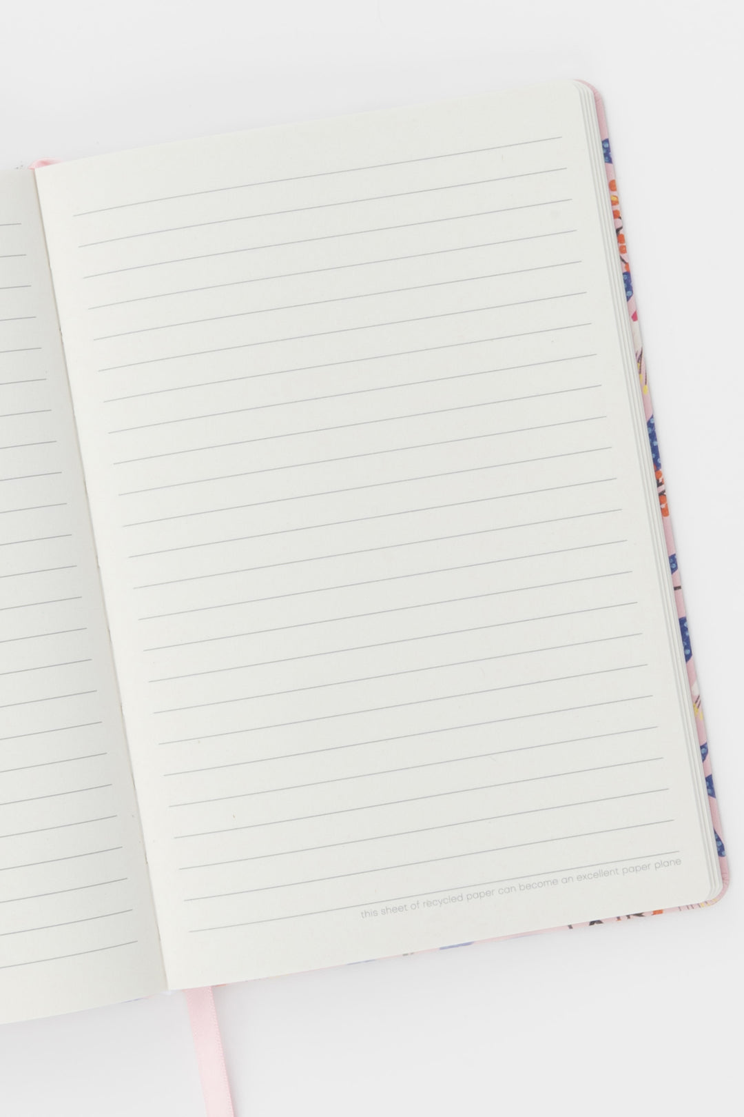 open notebook showing ruled pages with the pink ribbon marker visible at the bottom
