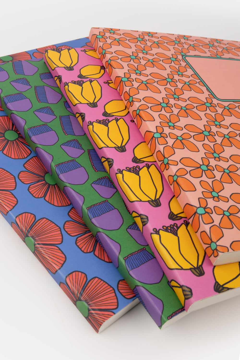 four colorful patterned notebooks stacked on a white background