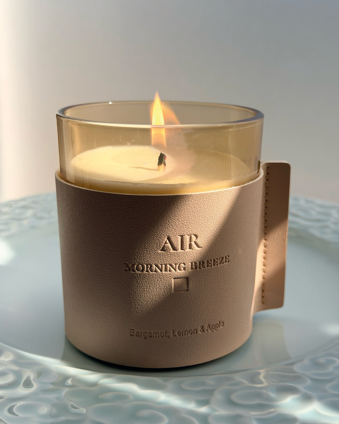 A yellow glass jar candle with white wax sits in a light beige faux leather sleeve
