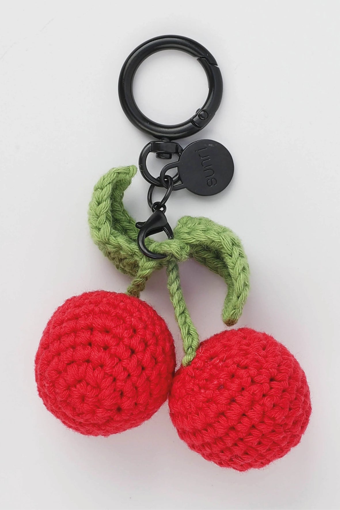 A pair of crocheted red cherries with green stems and leaves, attached to a black metal key ring and clasp, on a plain white background.