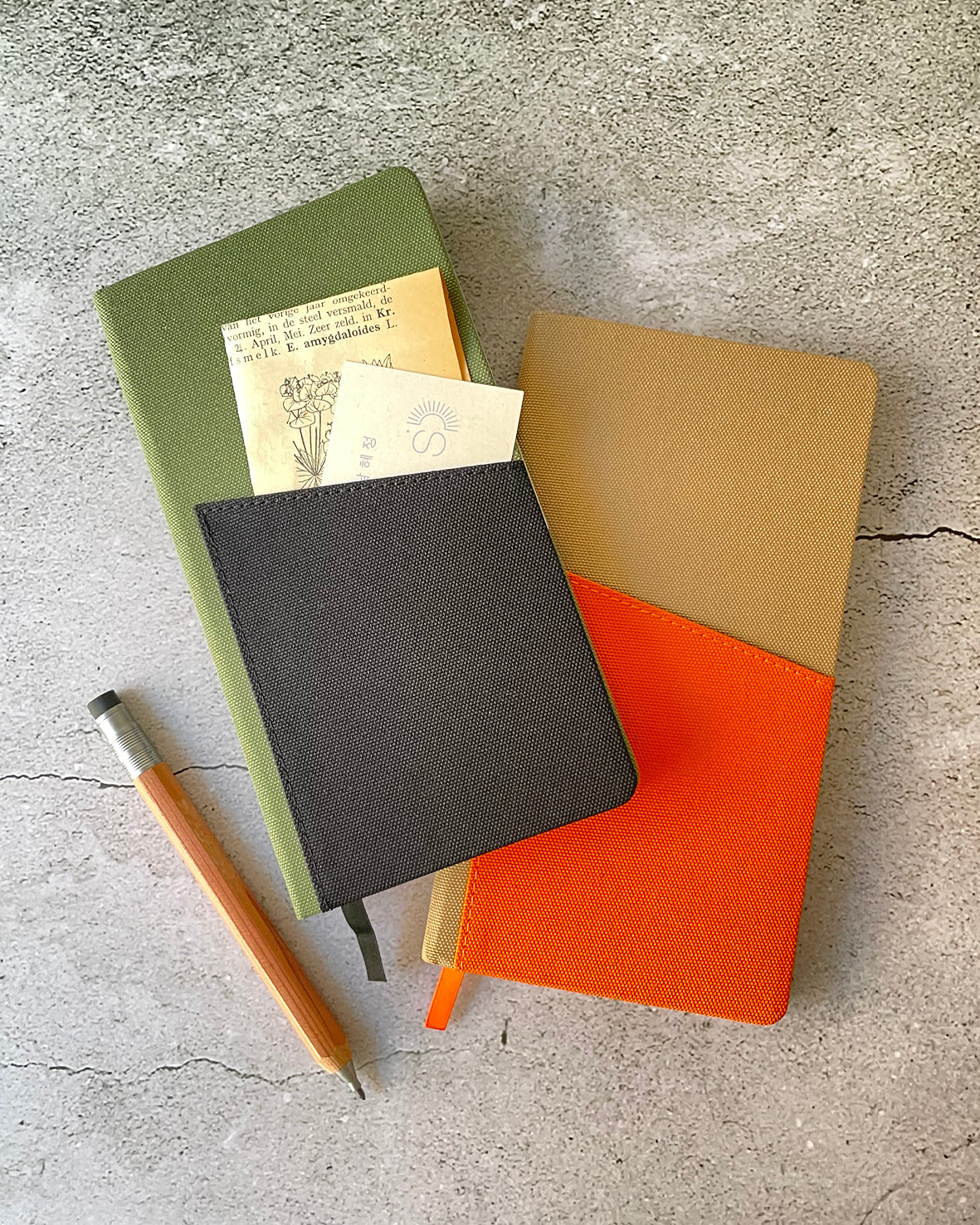 a green and black pocket size sketchbook and a orange brown pocket siza sketchbook on a grey background