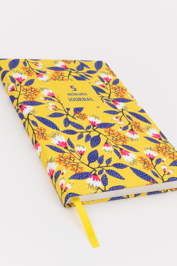 angled view of a5 five minute journal with yellow floral fabric cover and ribbon marker
