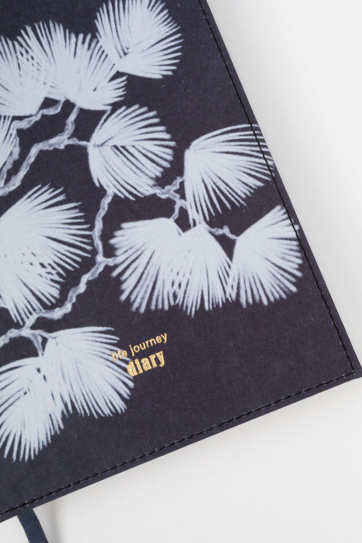 A5 diary cover detail with white botanical illustration on dark fabric surface