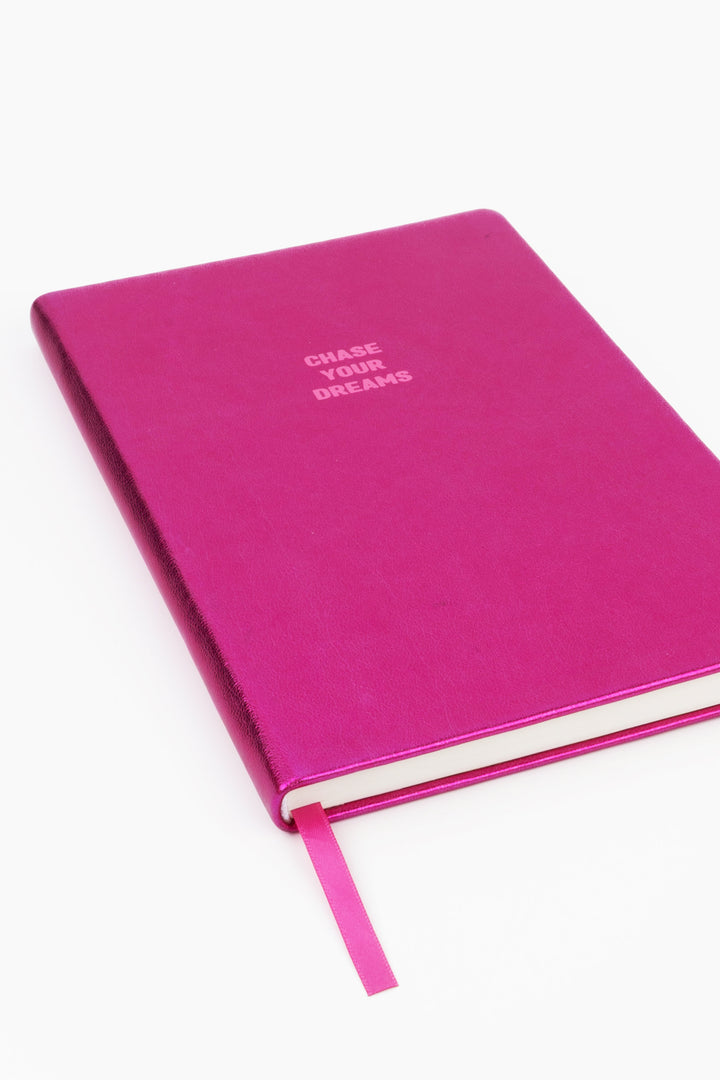 Angled view of closed pink metallic A5 notebook with chase your dreams text and pink ribbon marker
