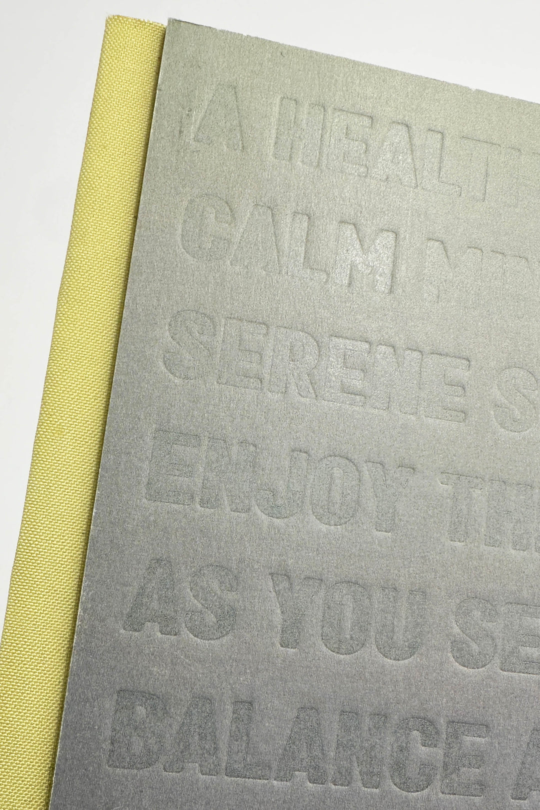 Grey notebook with embossed text and yellow spine on a white background