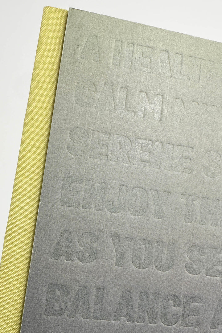 Grey notebook with embossed text and yellow spine on a white background