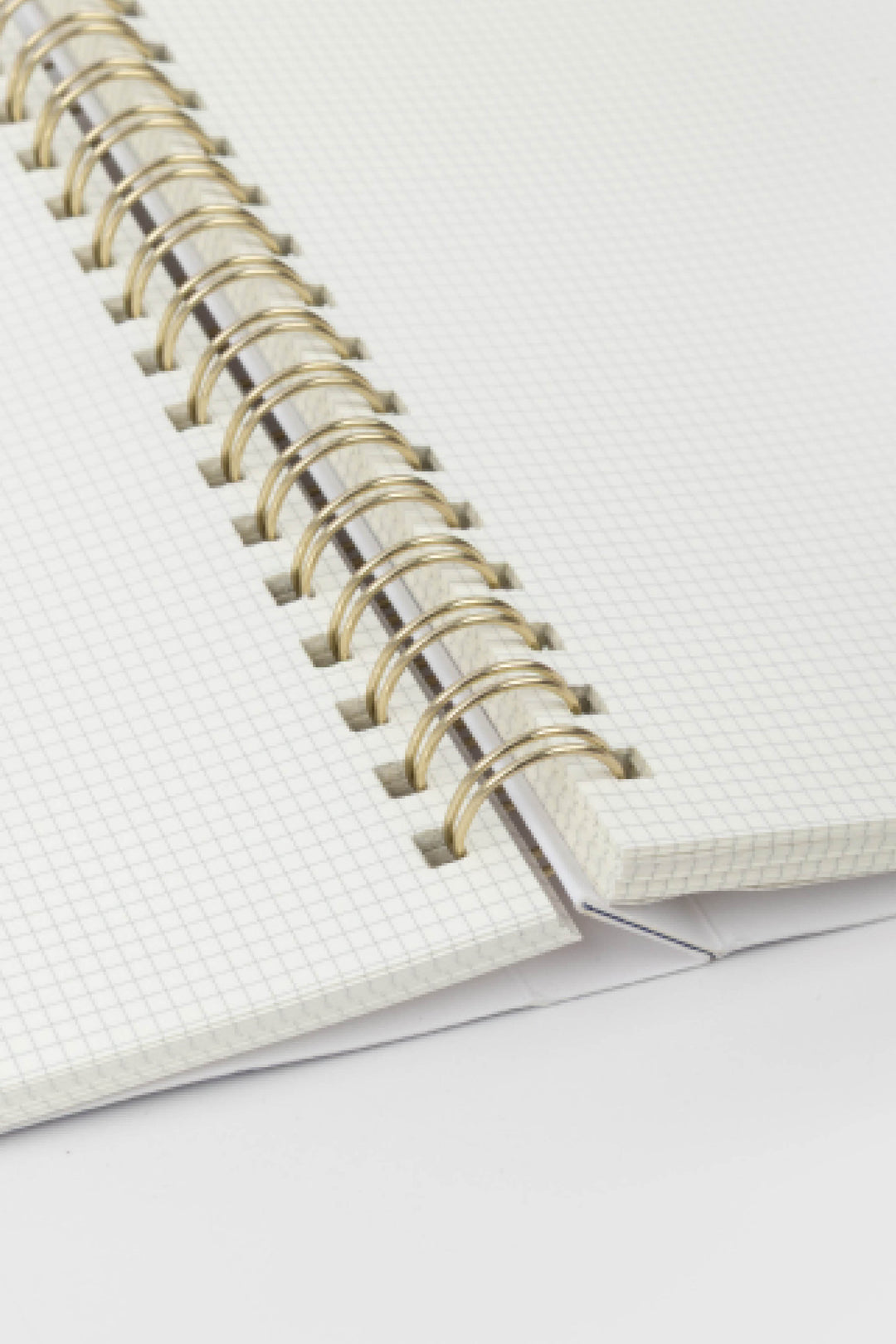 Close-up of a notebook with a white cover and gold spiral binding on a light gray background.