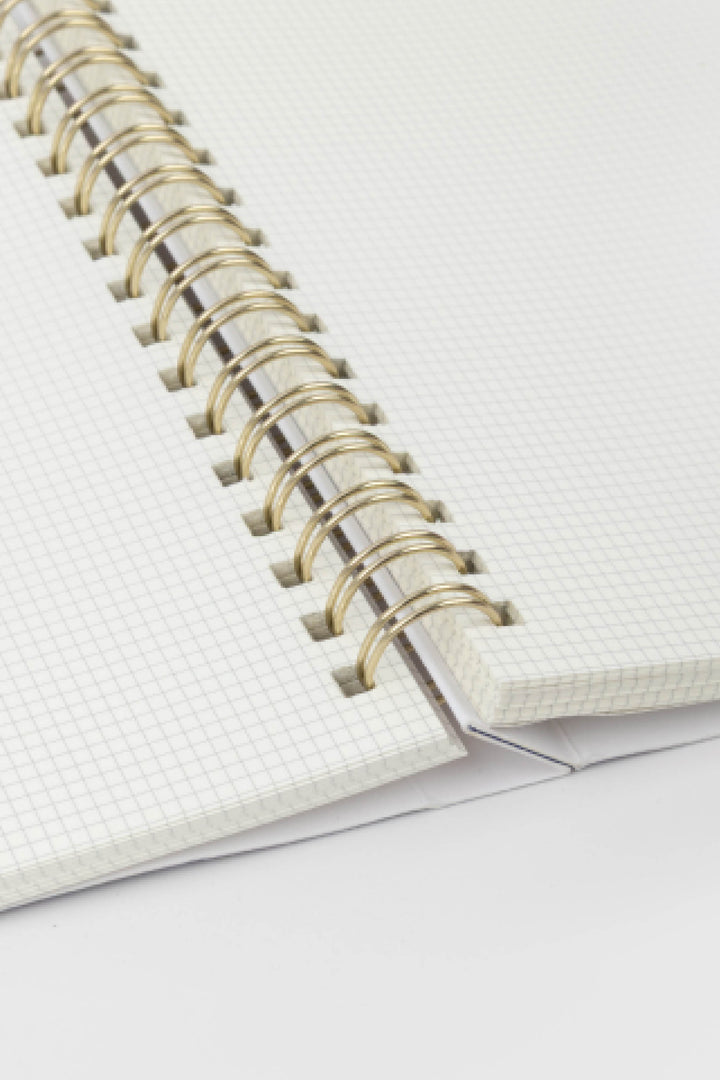Close-up of a notebook with a white cover and gold spiral binding on a light gray background.
