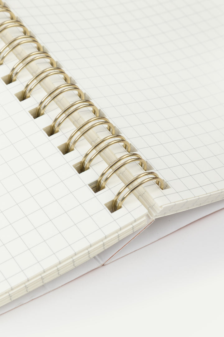 Close-up of open A5 notebook pages with a 5mm grid pattern and gold wire-o binding
