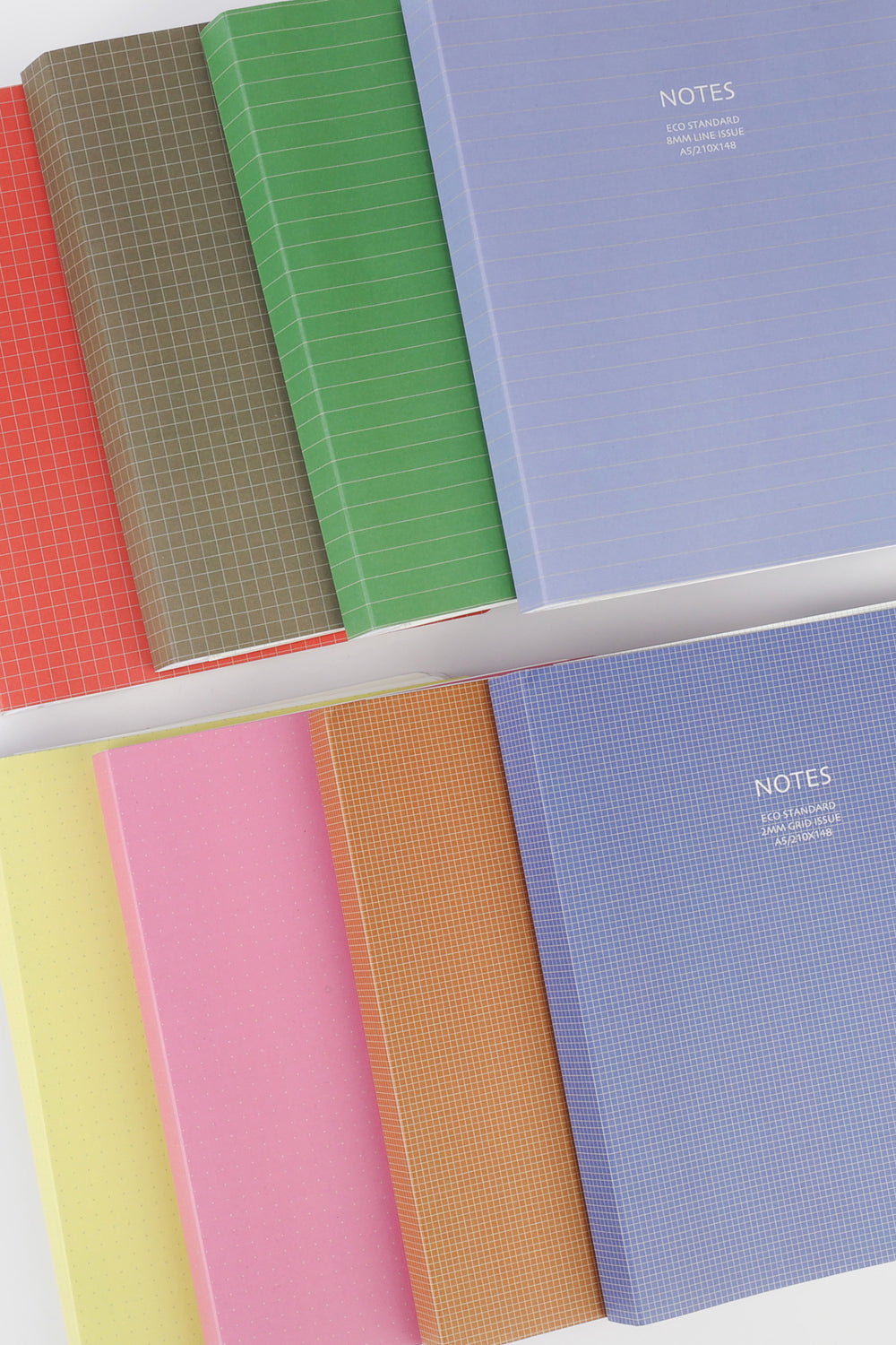assorted eco notebooks in multiple colours arranged in a layered flatlay showing different cover patterns
