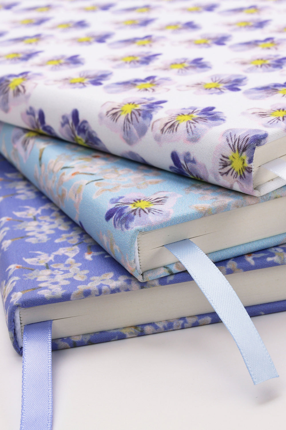 Stack of floral-patterned notebooks with ribbons on a white background