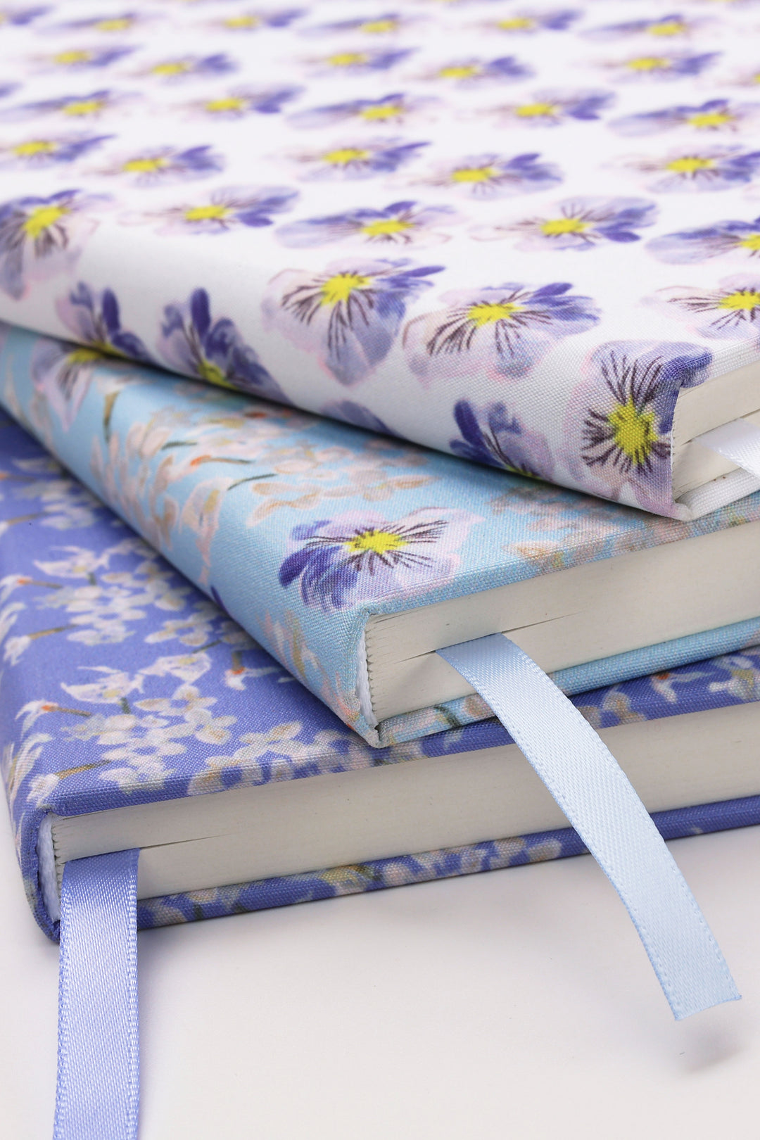 Stack of floral-patterned notebooks with ribbons on a white background