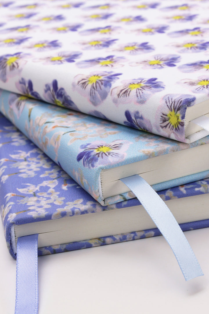 Stack of floral-patterned notebooks with ribbons on a white background