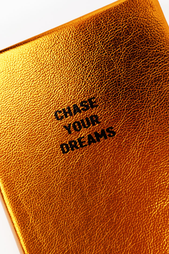 Close-up of the A6 metallic orange notebook cover showing the Chase Your Dreams text