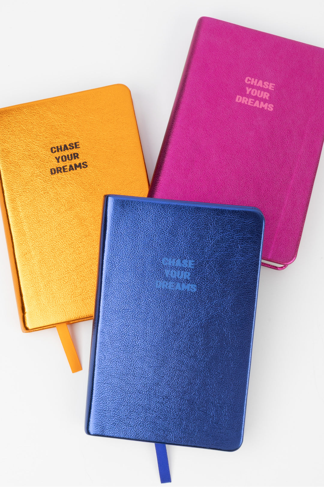 Three metallic notebooks in orange pink and blue arranged together with visible chase your dreams text
