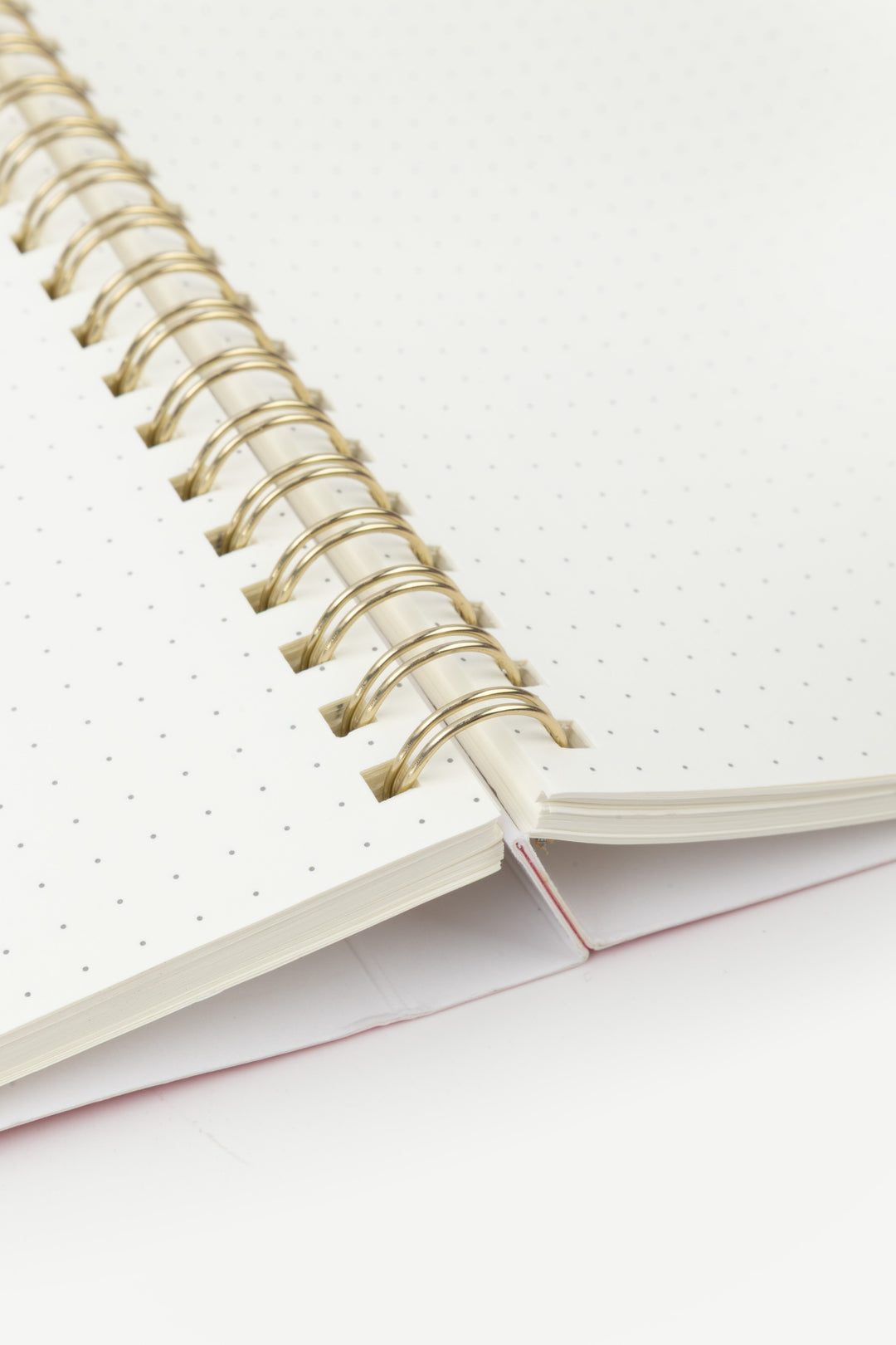 Close-up of a spiral-bound notebook with white pages on a light pink background