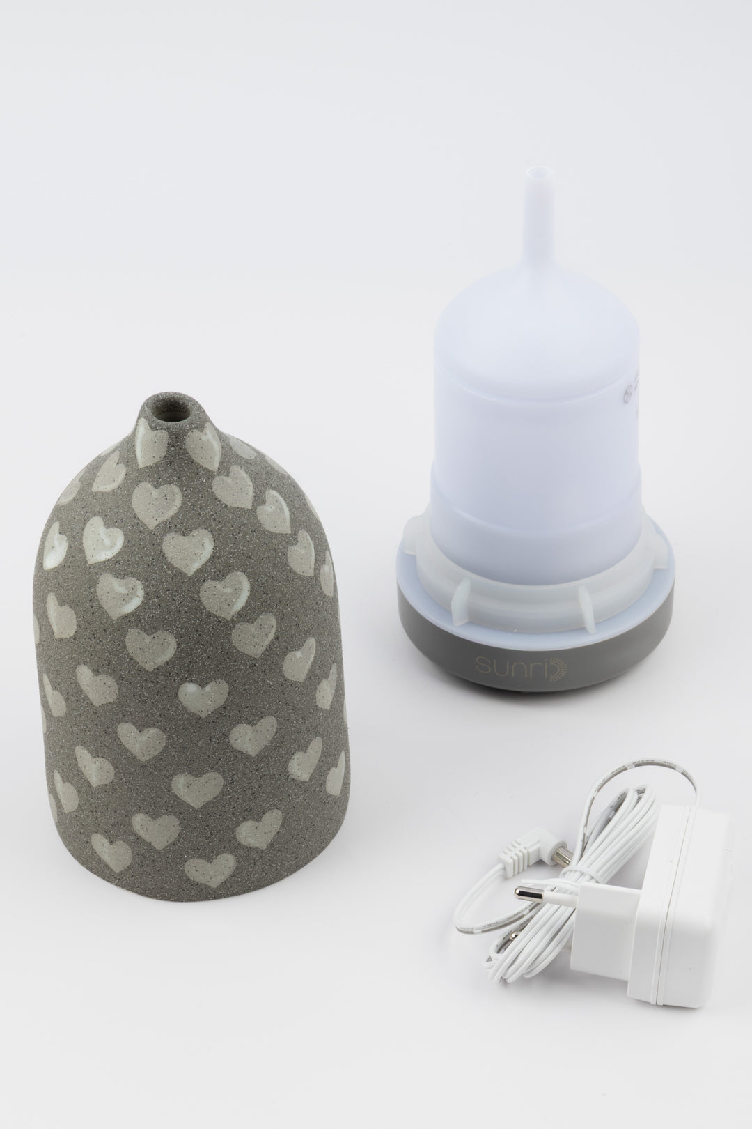 Grey vaporiser with heart patterns and a white container and charging cable on a light gray background
