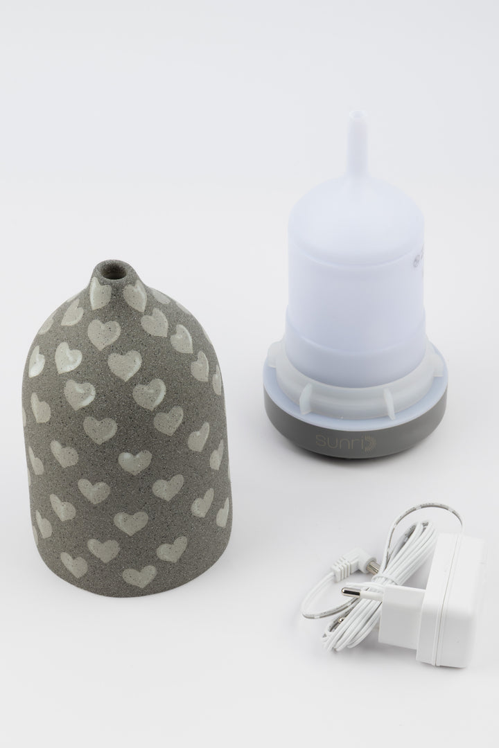 Grey vaporiser with heart patterns and a white container and charging cable on a light gray background