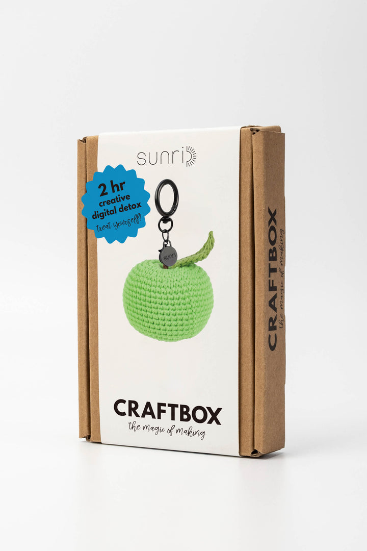 Craft box with a green crocheted apple keychain on a white background