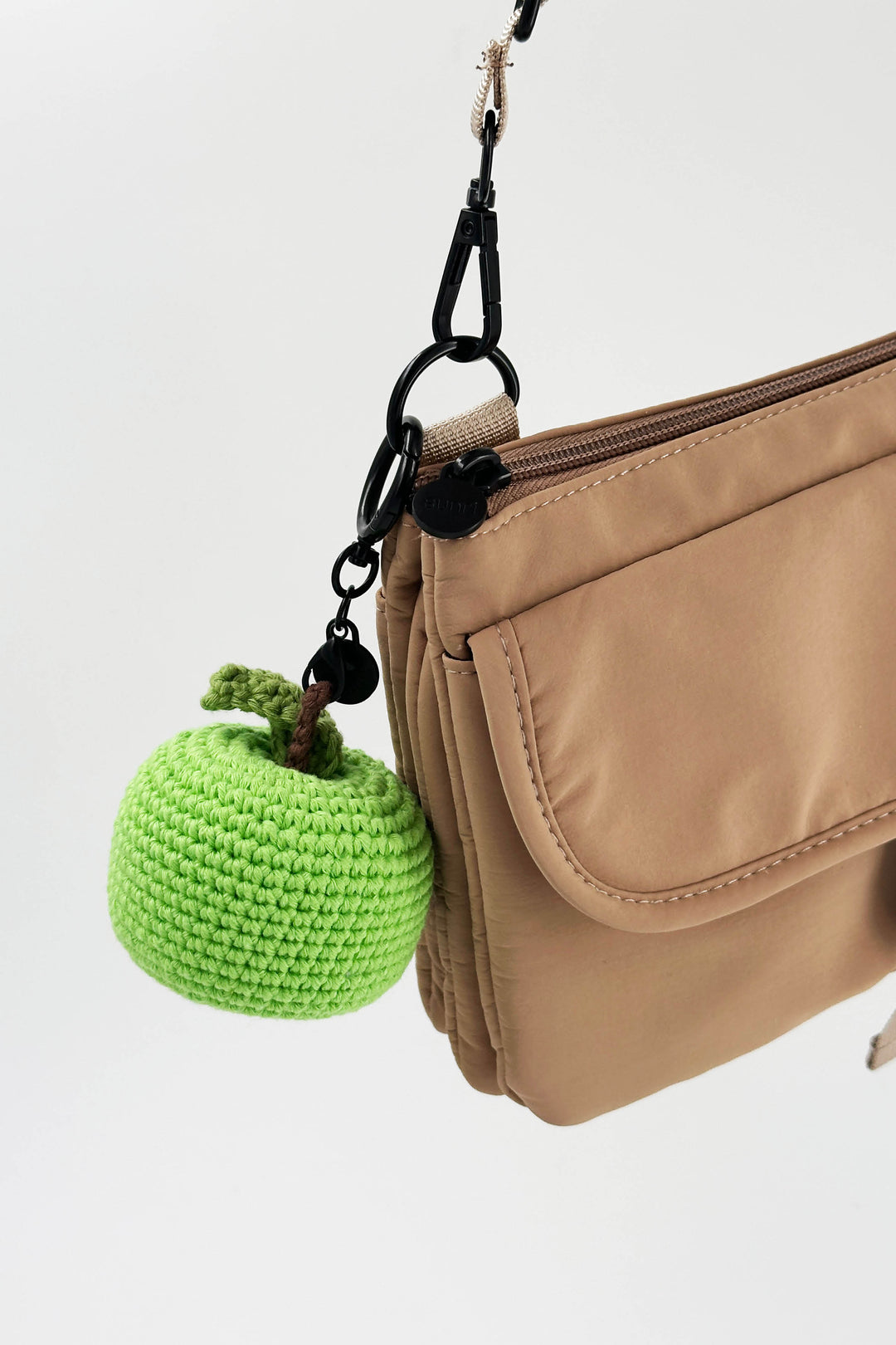 Beige handbag with a green knitted apple charm on a white background