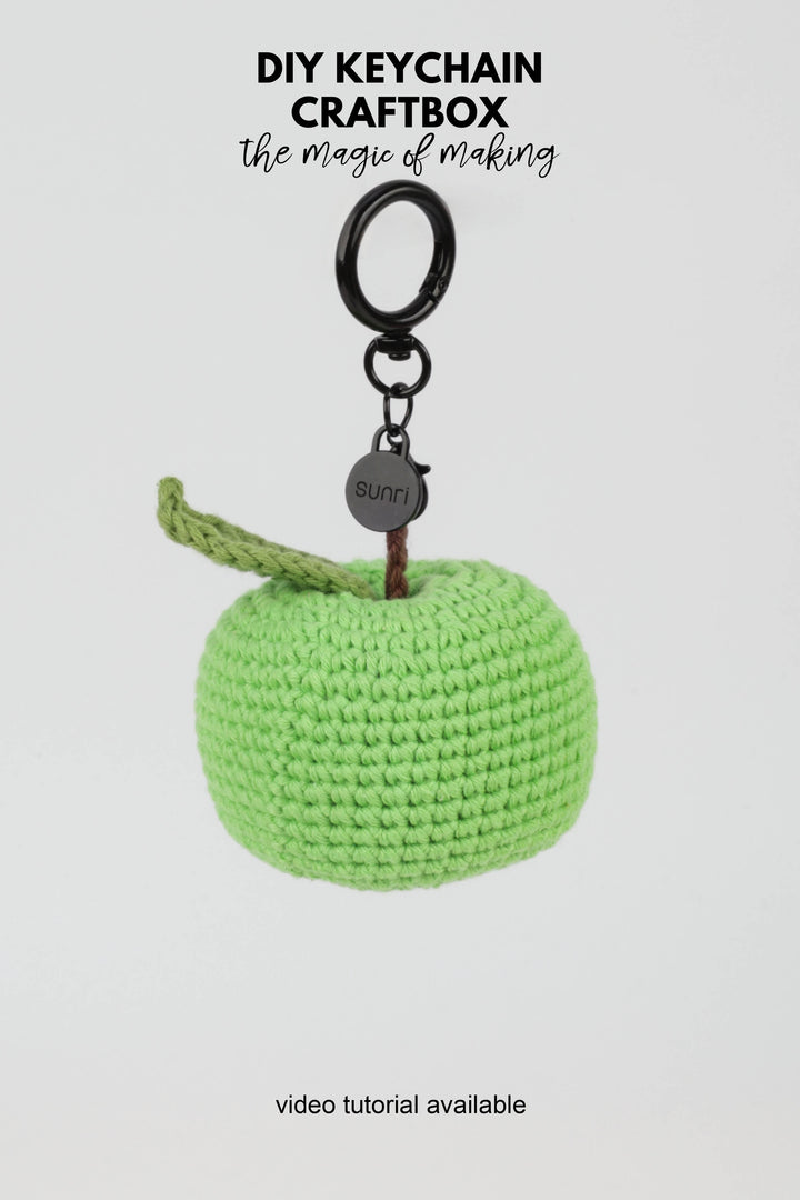 Green crocheted keychain with a black ring on a white background, featuring text about DIY keychain craftbox.