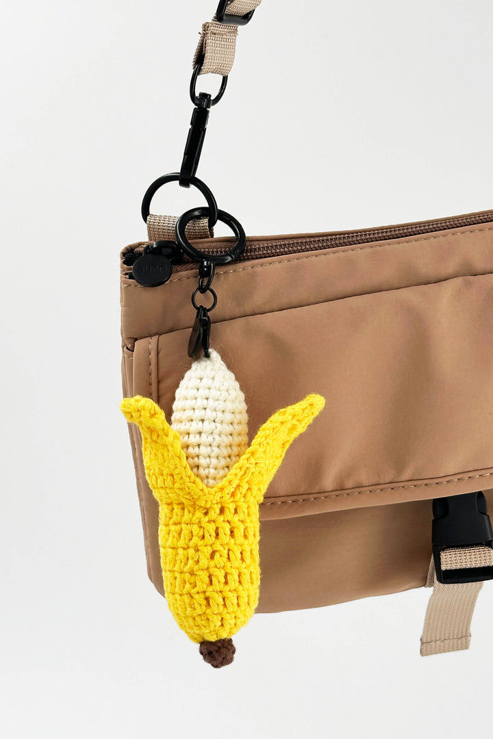 Crocheted banana keychain attached to a beige bag on a white background