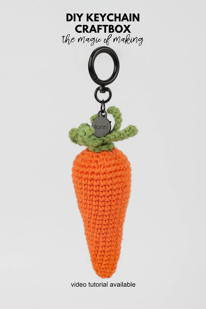 Crocheted carrot keychain with green top on a white background, featuring 'DIY Keychain Craftbox' text.