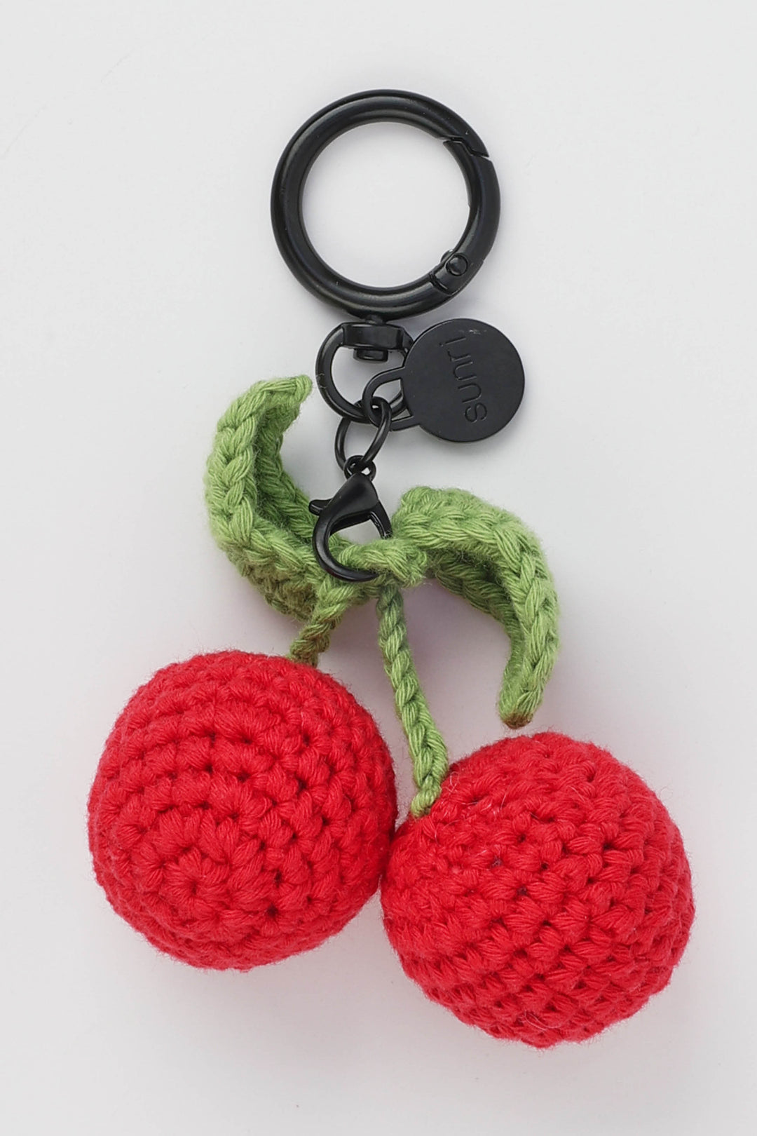 Crocheted cherry keychain with green stem on a white background