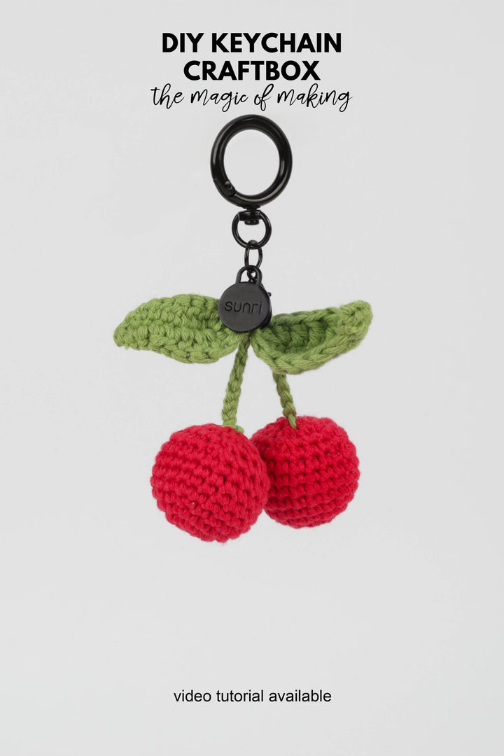 Crocheted cherry keychain with green leaves on a white background, featuring 'DIY Keychain Craftbox' text.
